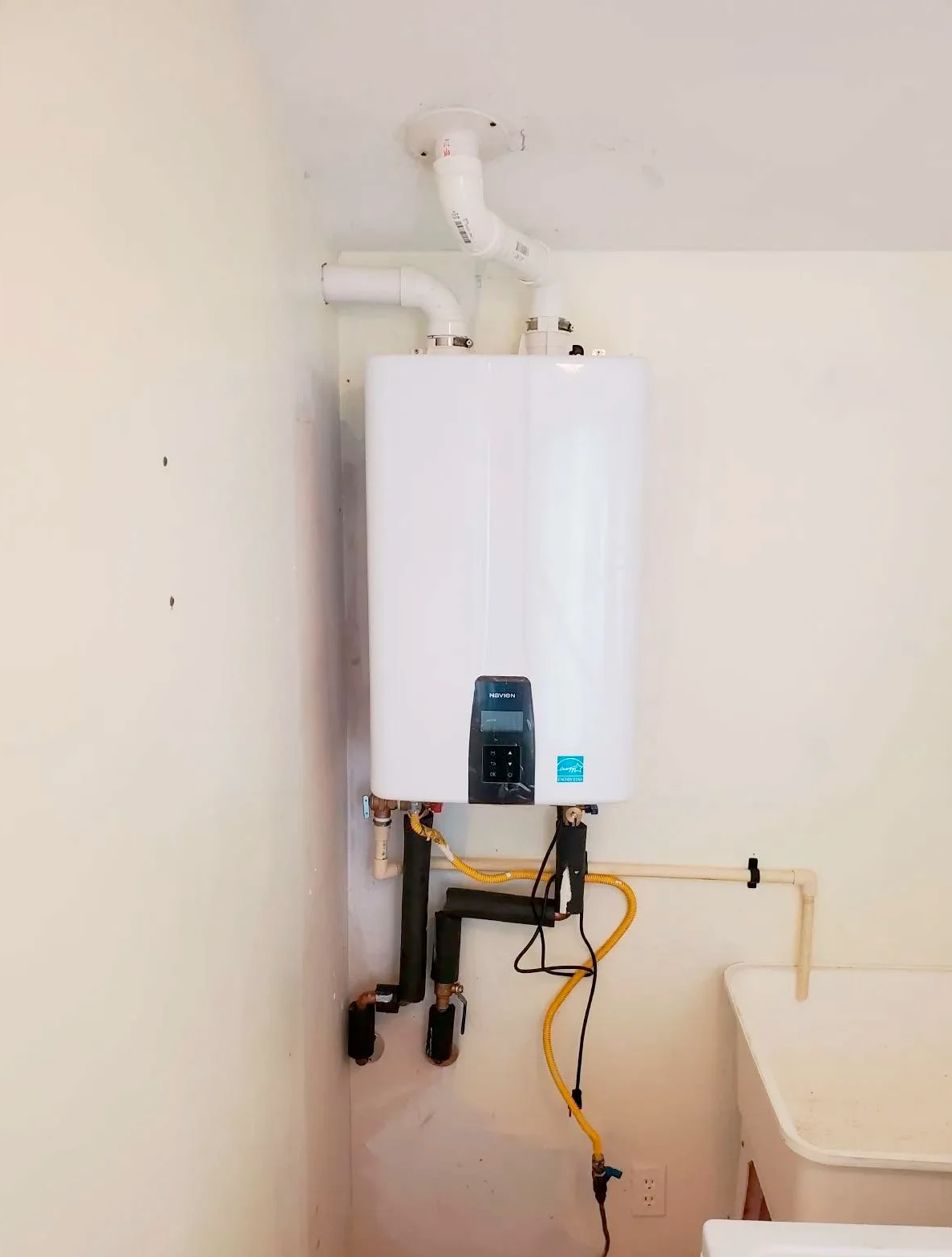 A white water heater is hanging on a wall next to a laundry sink.