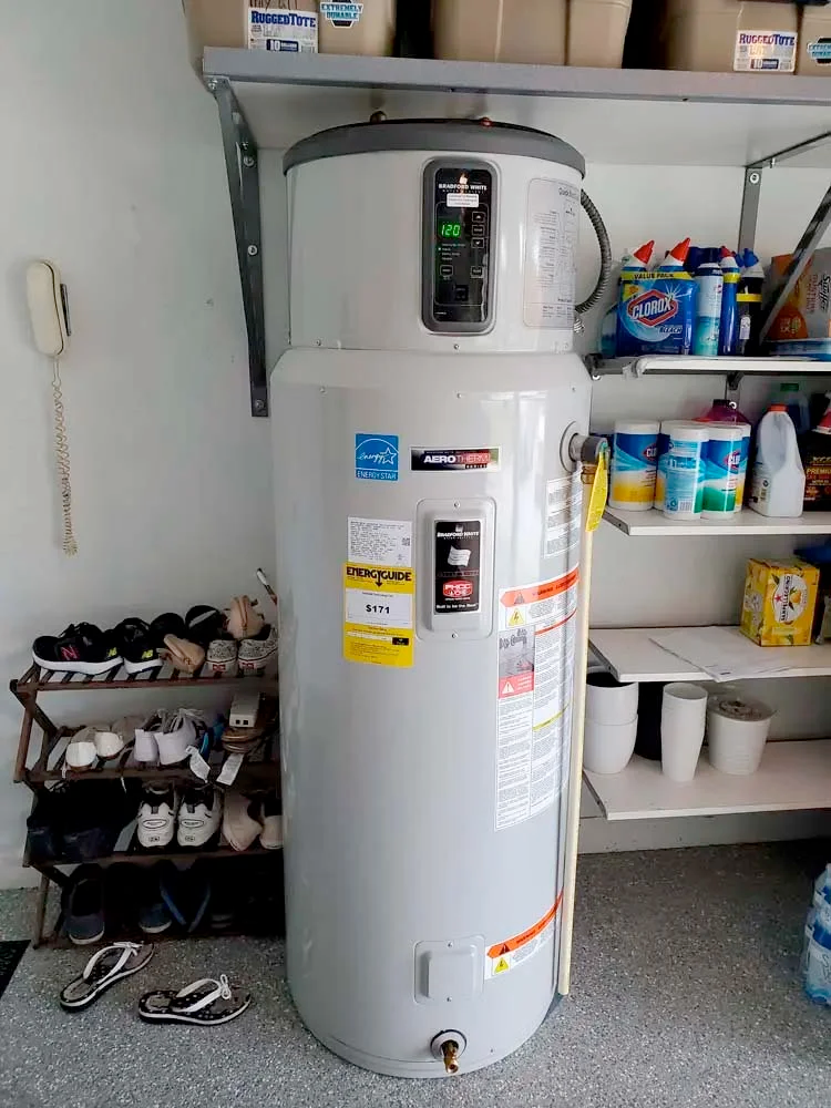 A water heater is sitting in a garage next to a shoe rack.