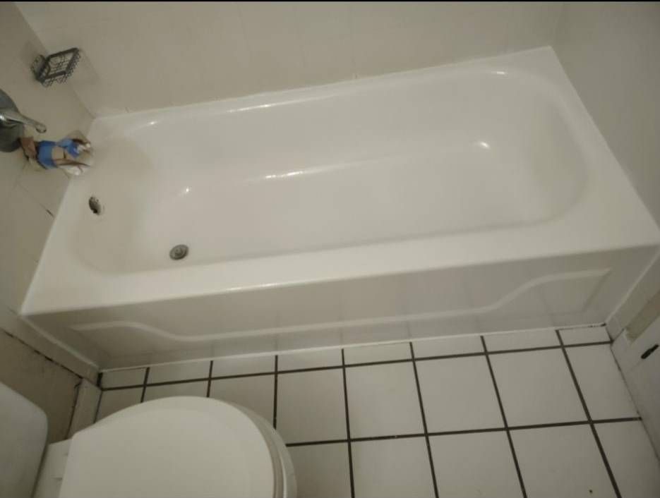 A white bathtub installed next to a toilet, positioned in a bathroom with white tiled flooring.
