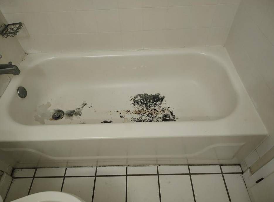 A dirty white bathtub containing dark, scattered debris, with a faucet and drain visible.
