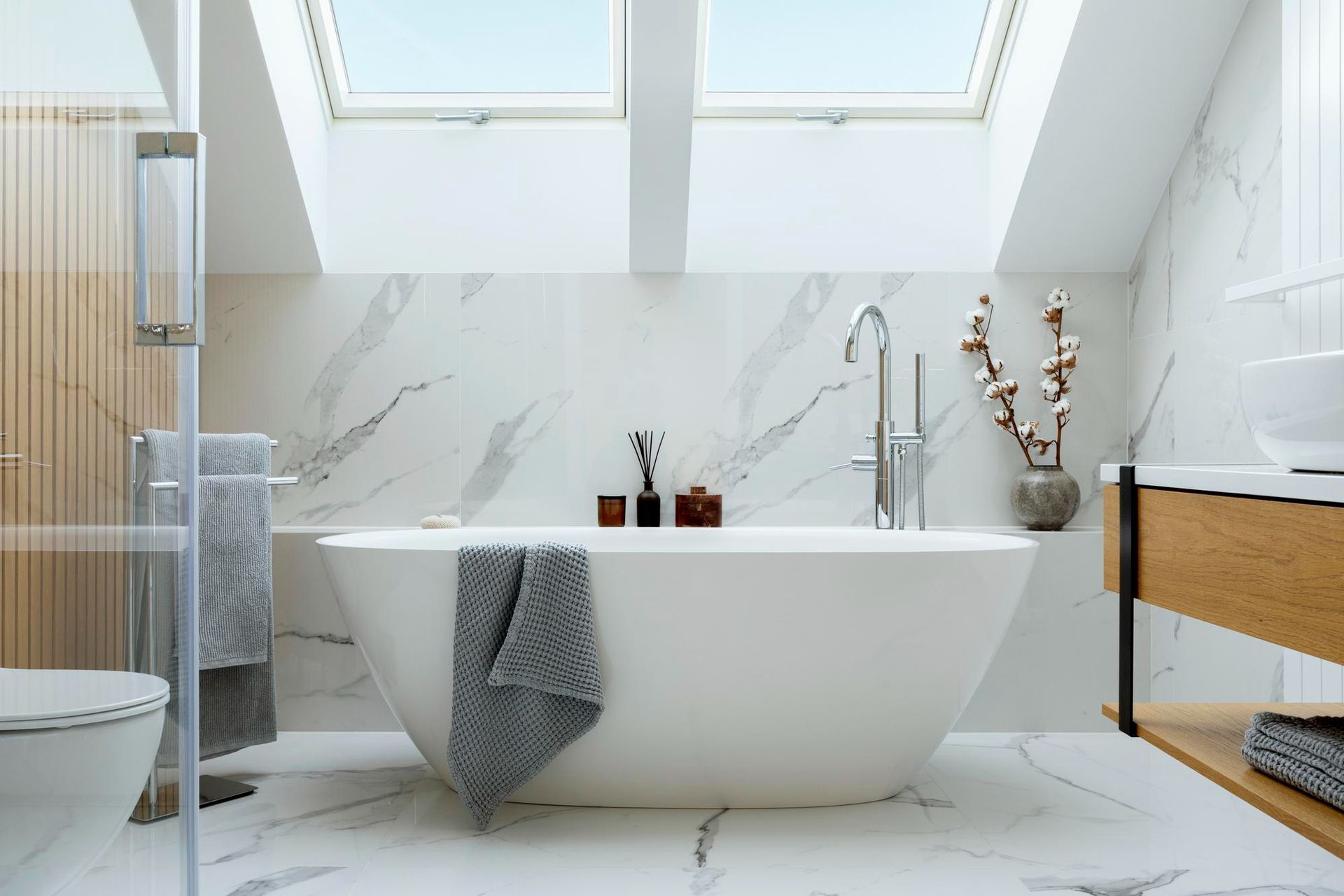 Bright, modern bathroom with white marble tile, soaking tub, and skylights.