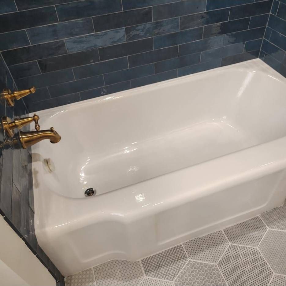 A white bathtub with vintage-style brass fixtures installed against a wall of dark blue rectangular tiles.
