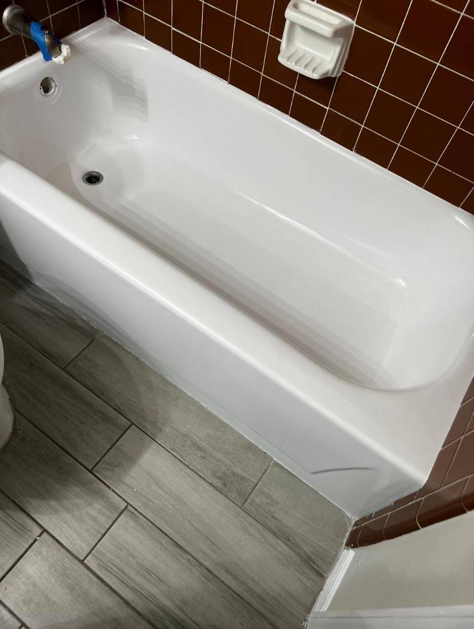 A clean white bathtub installed against dark brown tiled walls, next to wood-look tile flooring.