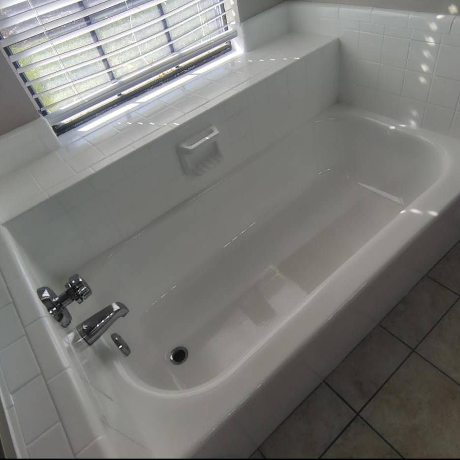 A white built-in bathtub with silver fixtures, tiled surround, and window blinds in a bathroom.