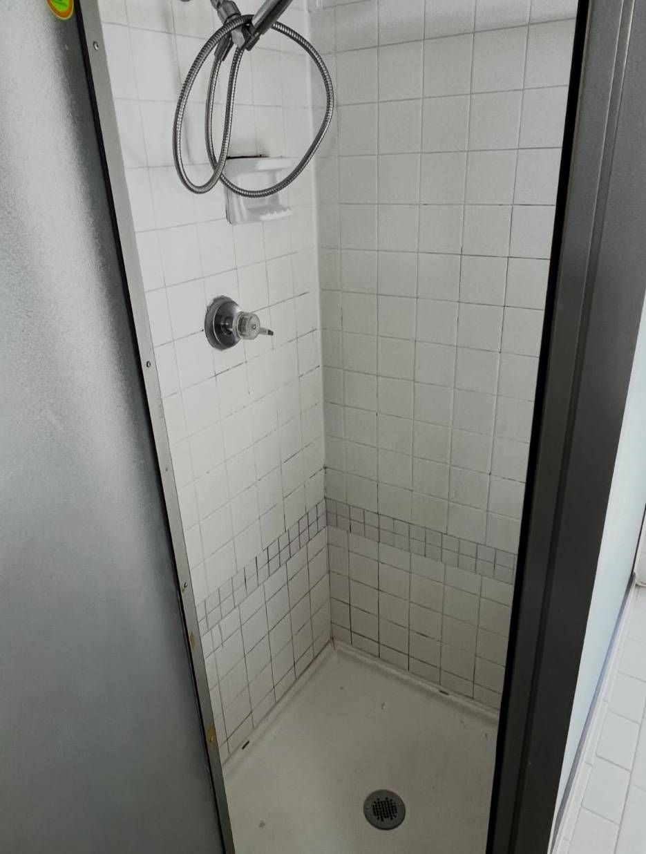A walk-in shower stall with white tiled walls, a silver shower head, and a white basin.
