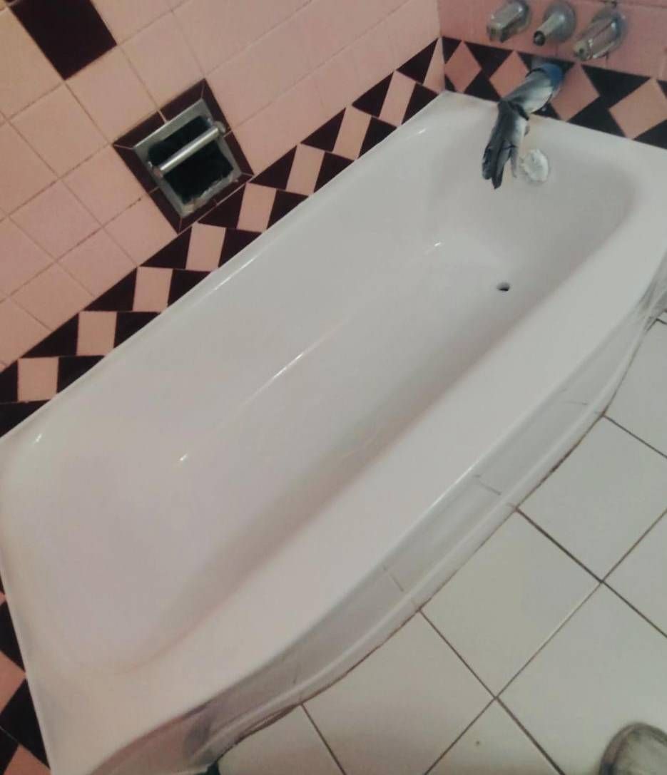 A white bathtub in a bathroom with pink and black diamond-patterned tiled walls and white floor tiles.