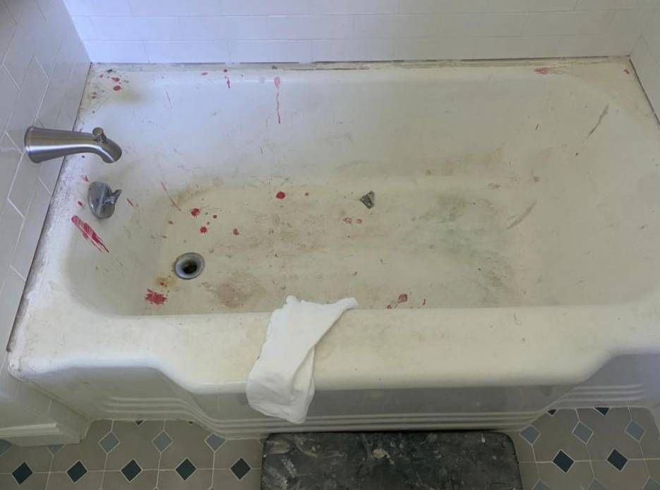 A stained, white bathtub in a bathroom with patterned tile floors and a white towel resting on the edge.