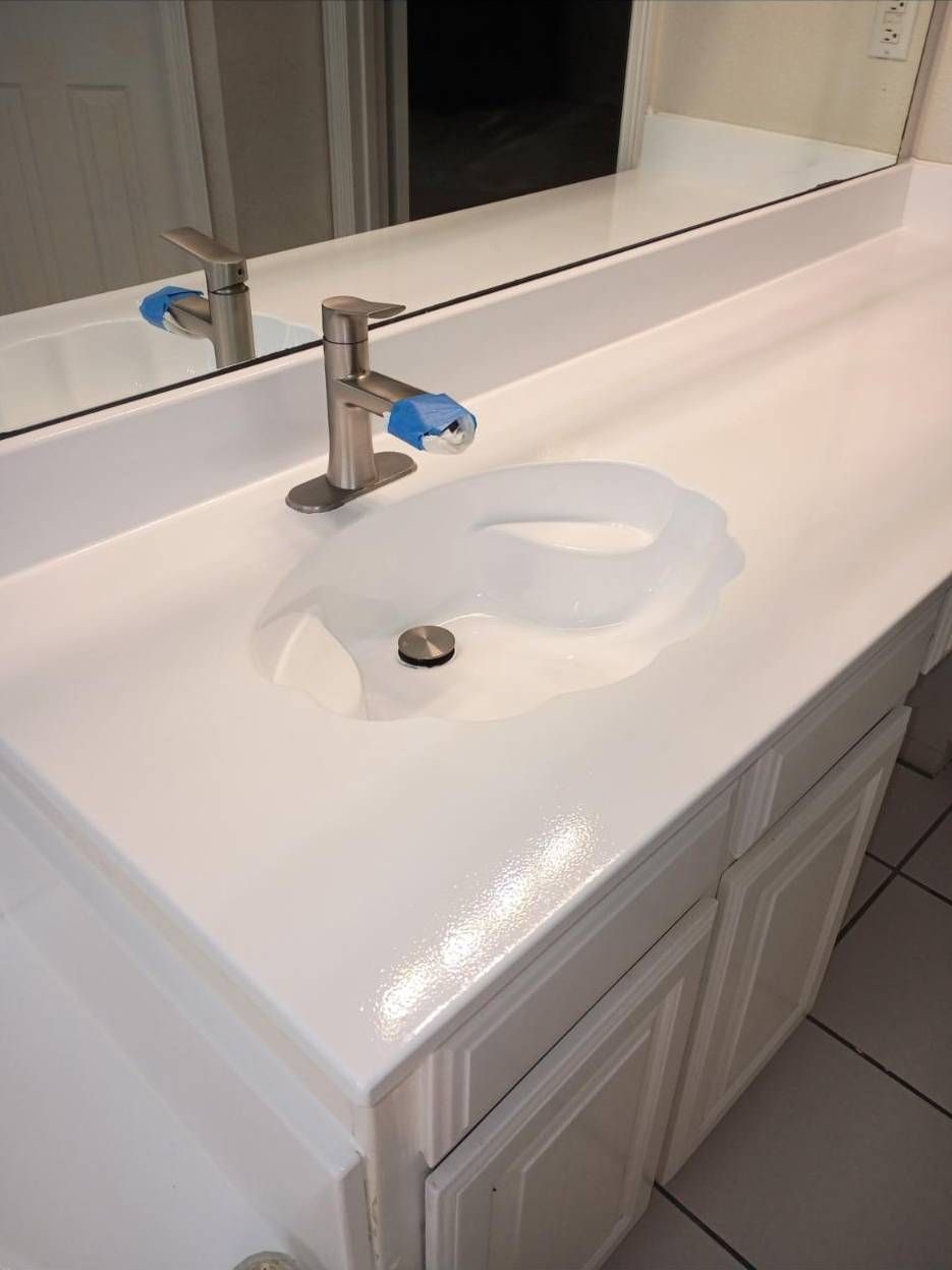 A clean white bathroom vanity with a silver faucet and drain, featuring blue painter's tape on the faucet handles.