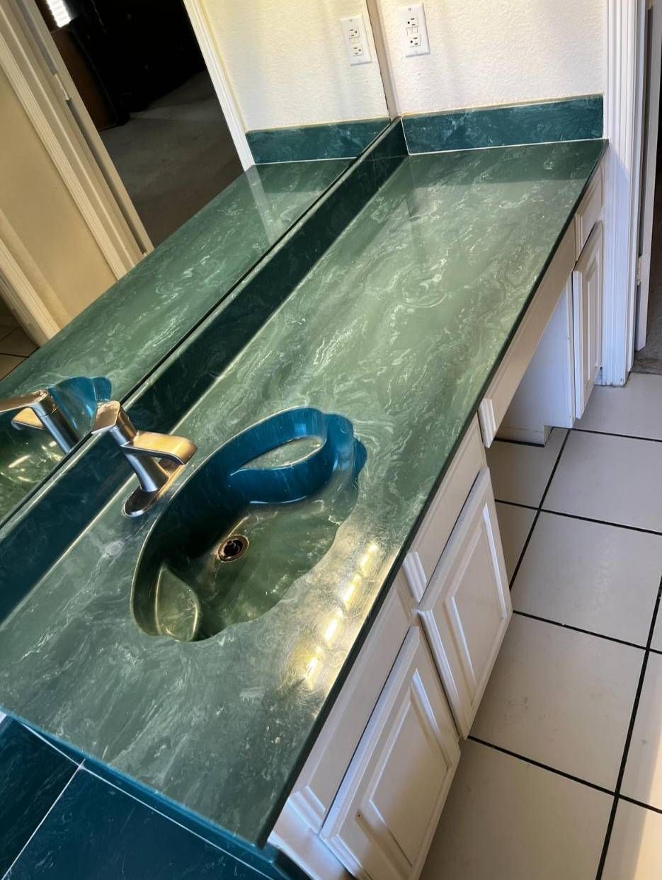 A bathroom vanity with a green faux-marble countertop, an integrated matching sink, and white cabinets.