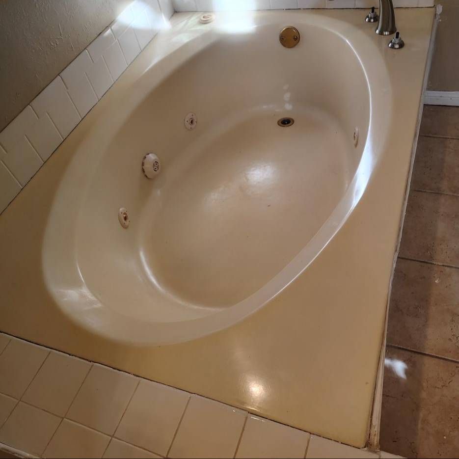 An oval jetted soaking tub in a tiled bathroom with a beige deck, white wall tiles, and neutral-toned floor tiles.