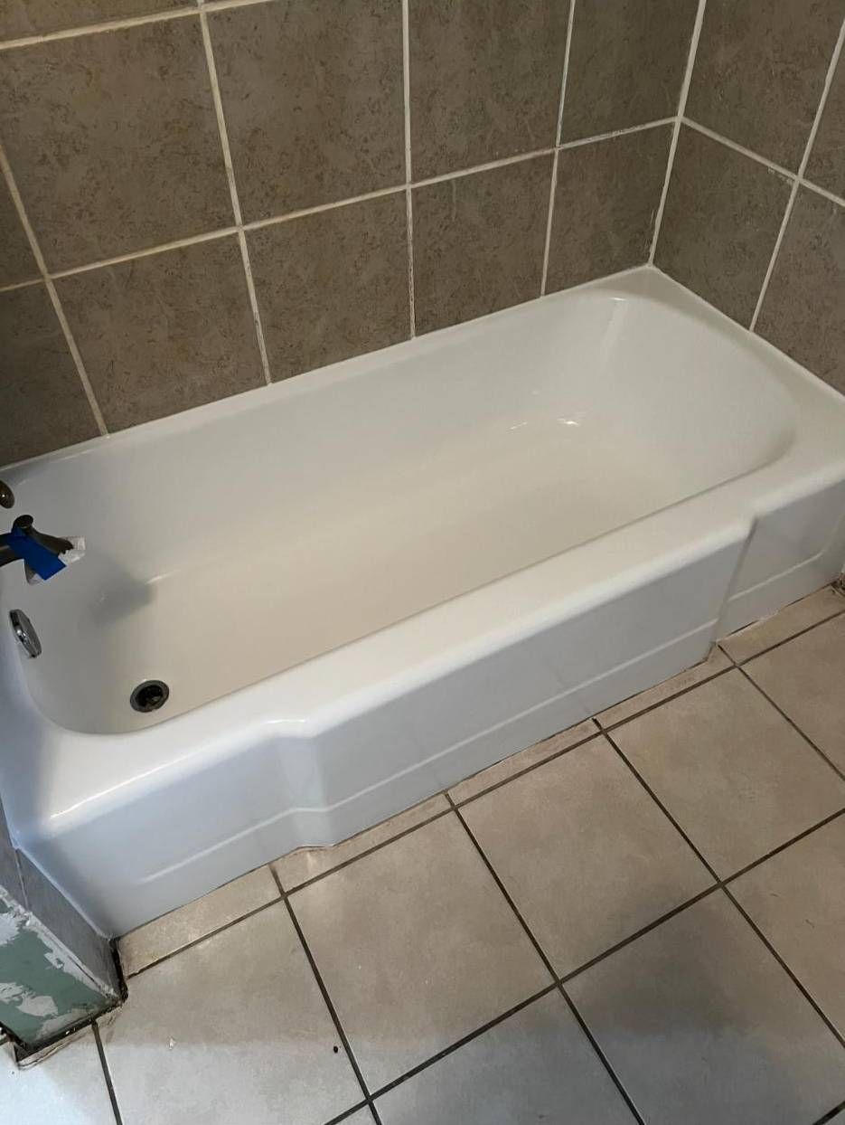 A white bathtub with a chrome faucet and drain, installed against tiled walls in a bathroom with tiled flooring.