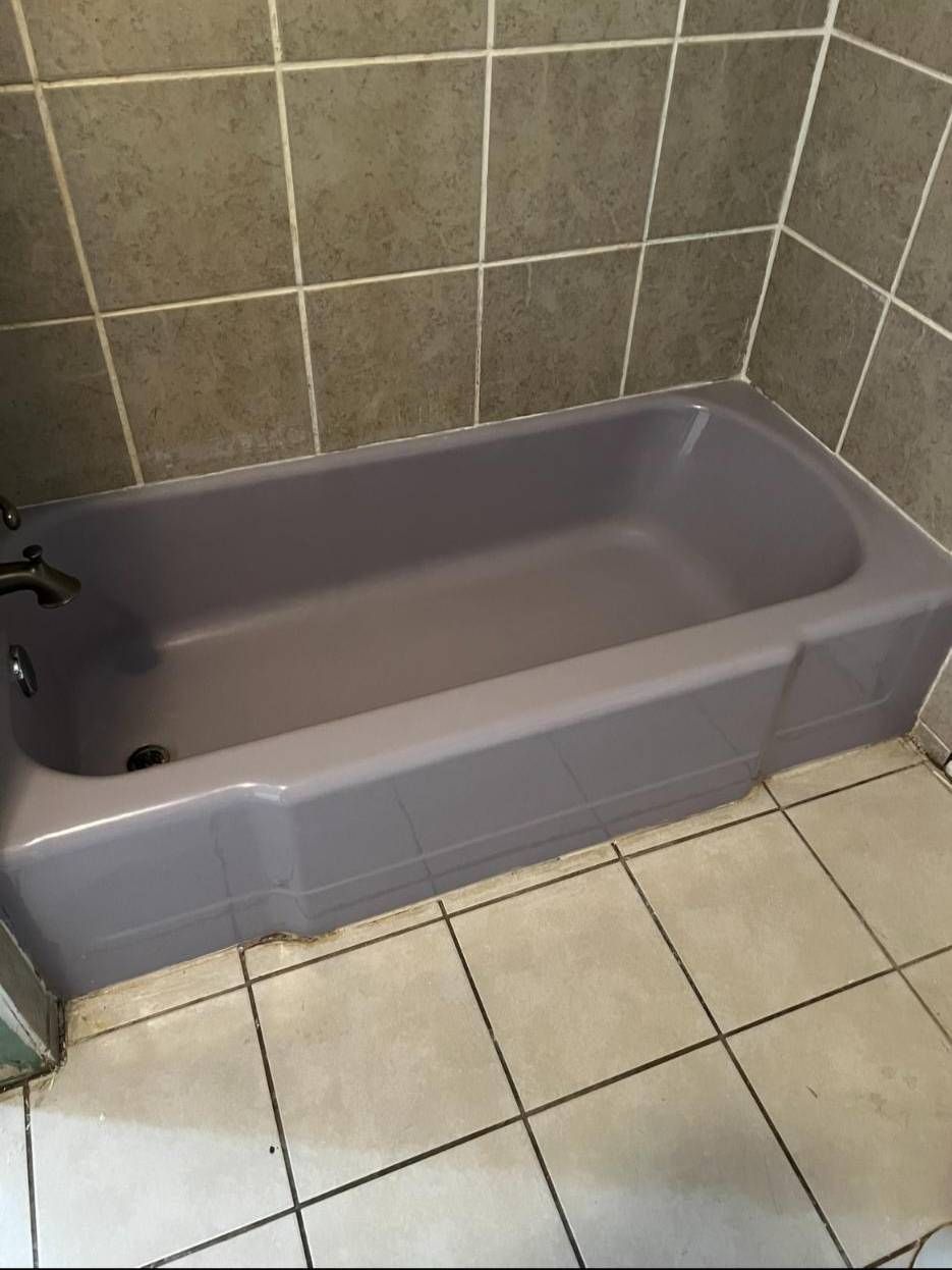 A gray bathtub installed in a bathroom with beige tiled walls and floors.