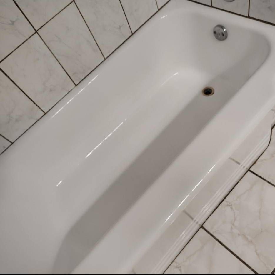 A white bathtub with silver fixtures, positioned in a bathroom with tiled walls and floors.