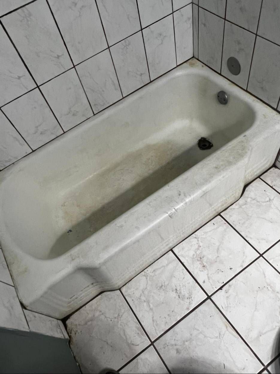 An overhead view of a stained, white bathtub surrounded by white tiled walls and floor in a small bathroom.