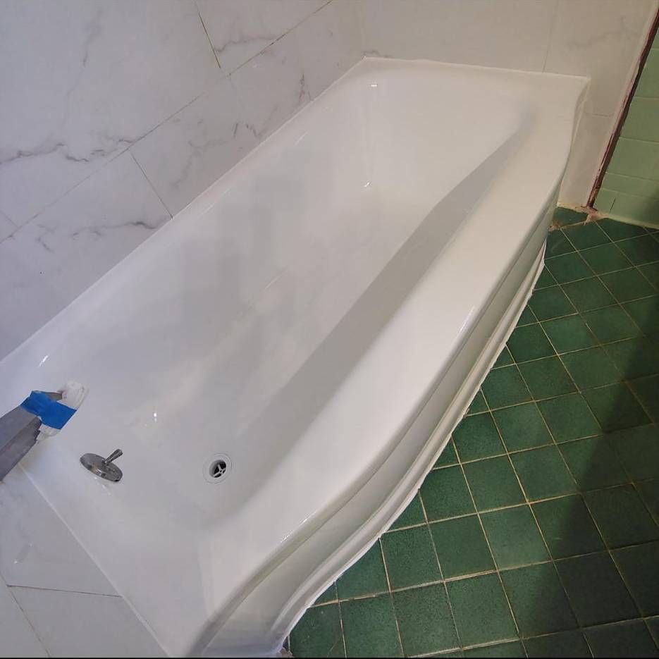 A white bathtub installed against marble-patterned walls and a floor with green square tiles.