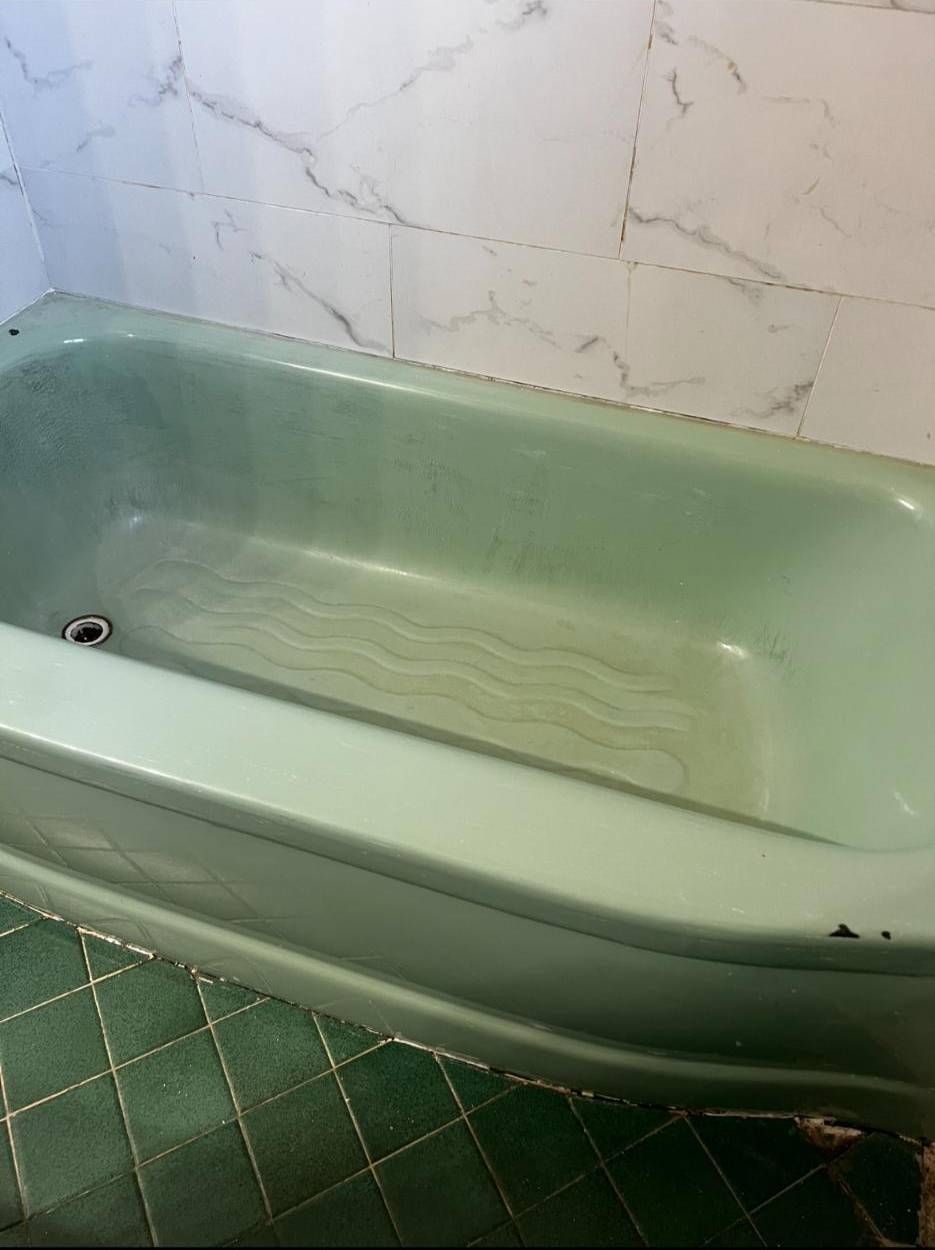 A vintage mint green bathtub with a wavy textured bottom, set against white marble-style tiled walls and green floor tile.