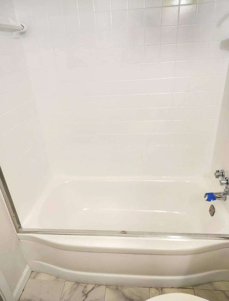 A white bathtub and shower surround with white subway tiles and a sliding glass door.