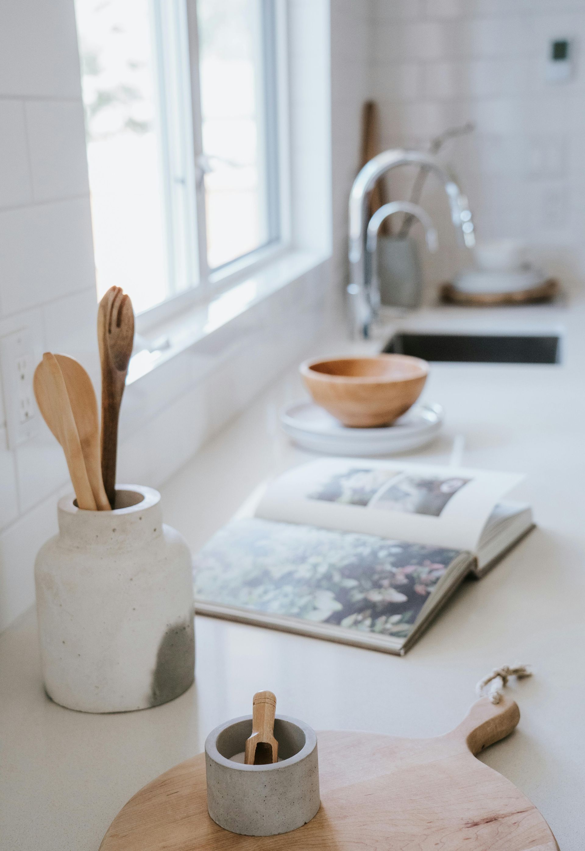 Kitchen counter with wooden utensils, cookbook, and a salt cellar by a window.
