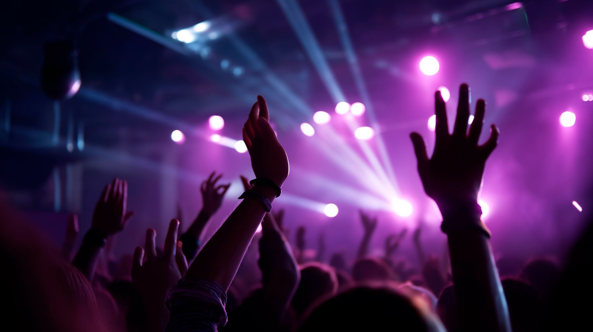 Social Club crowd with raised hands under purple stage lights and beams dancing to music played by DJ Kerry Balearic