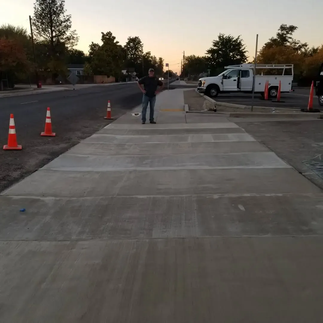 Freshly repaired concrete sidewalk with safety cones and a worker standing nearby in San Diego.