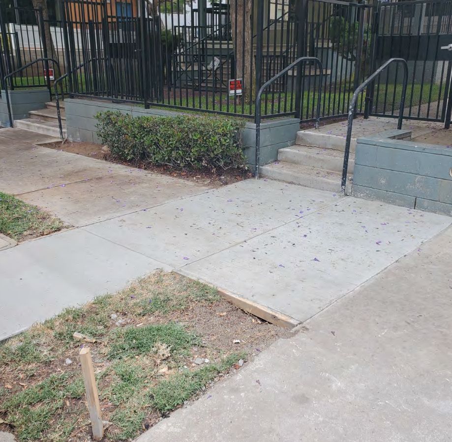 A man is spreading concrete on a sidewalk with a trowel.