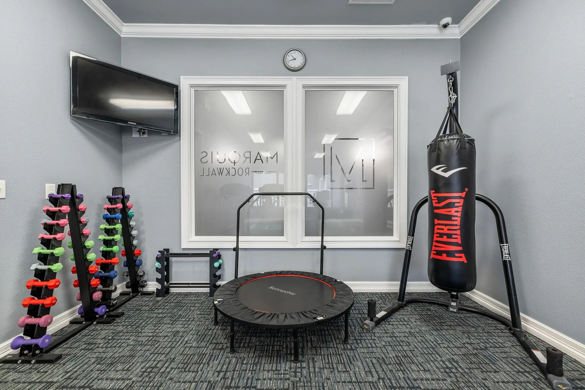 Fitness room with dumbbells, punching bag, trampoline, and TV.
