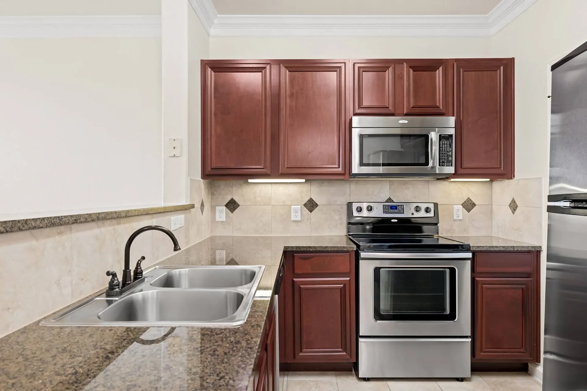 Kitchen with dark wood cabinets, granite countertops, stainless steel appliances including a microwave, stove, and refrigerator, and a double sink.