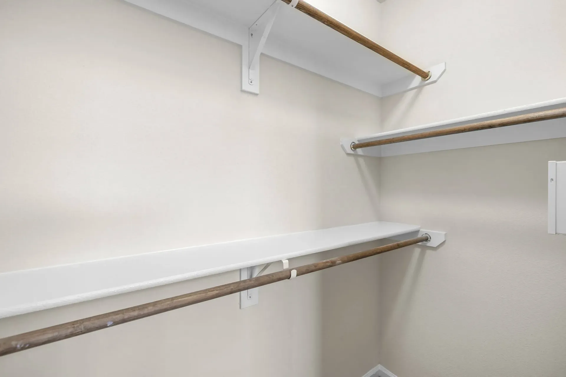 Empty walk-in closet with white shelves and wooden hanging rods.