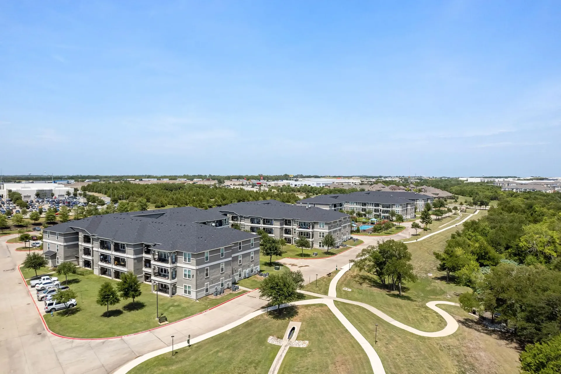 Aerial view of modern apartment buildings with surrounding green spaces and a swimming pool.