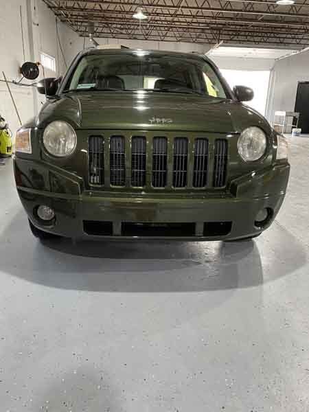 A green jeep compass is parked in a garage.