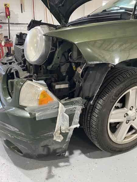 A green car with its hood open is sitting in a garage.