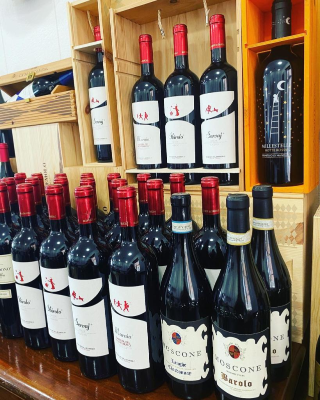 Bottiglie di vino in un negozio, per lo più rosse con etichette rosse. Scatole di legno e scaffali contengono le bottiglie in esposizione.