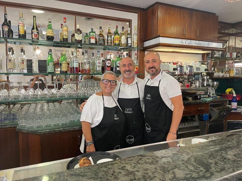 Tre persone sorridenti dietro un bancone. Il bancone è pieno di bottiglie e bicchieri.