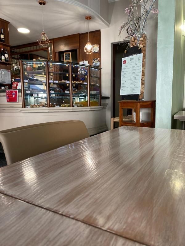 Interno di un bar con un tavolo di legno in primo piano. Vetrina con dolci sullo sfondo.