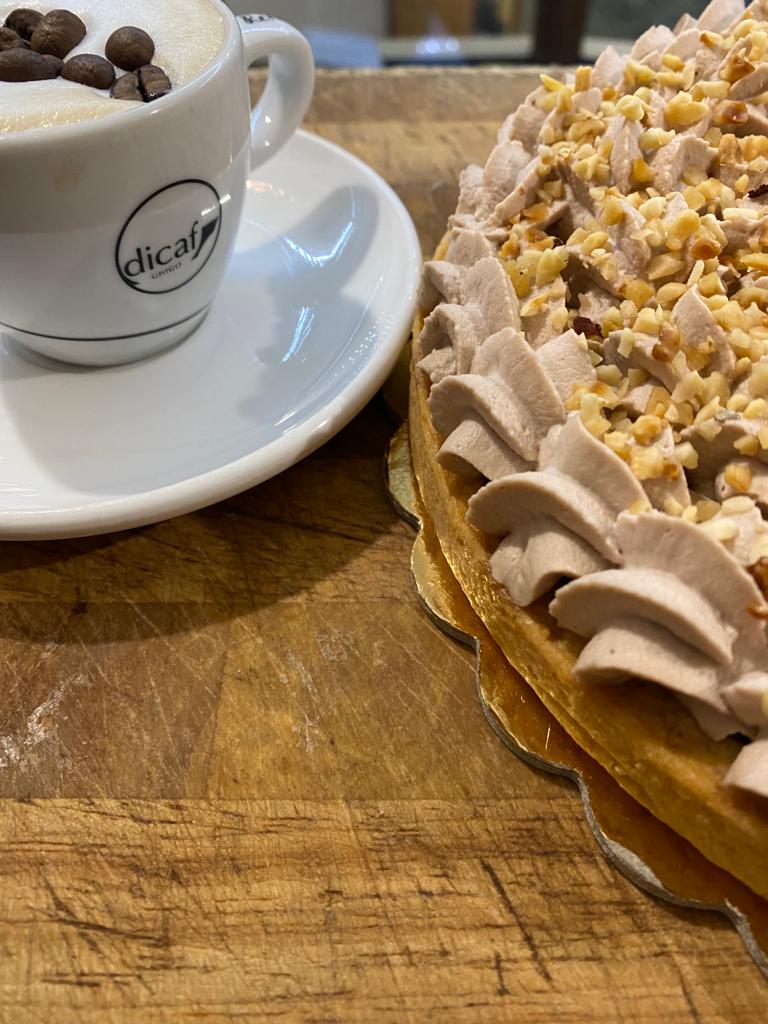 Tazza di cappuccino con chicchi di caffè e pasticcini su una superficie di legno.