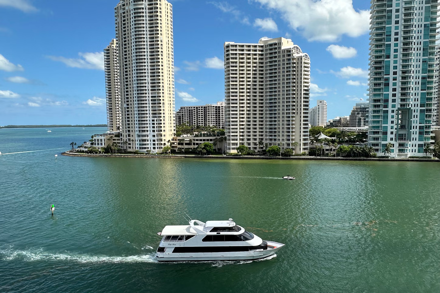 Boat on water, skyscrapers in the background. Blue water, sunny day, white and black boat, buildings.