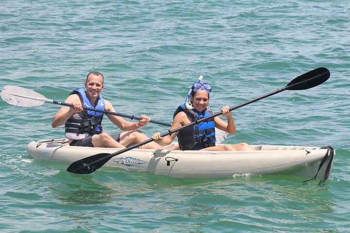 Two people kayaking in the ocean; the woman wears a snorkel, both are smiling, and wear life jackets.