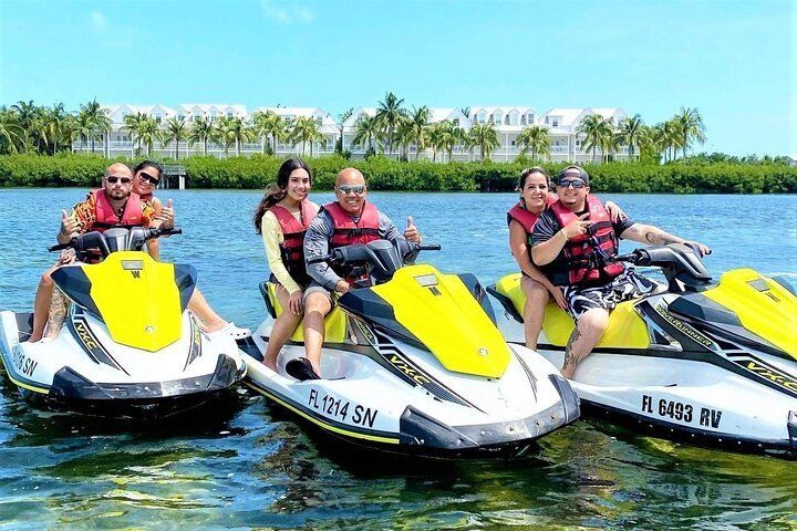 People on jet skis enjoying the water in front of a resort on a sunny day.