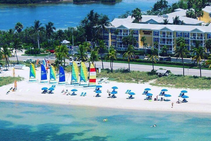 Beach with sailboats, umbrellas, and a resort in the background.