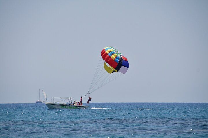 Boat towing a parasailer over a blue sea under a clear sky; colorful parasail.