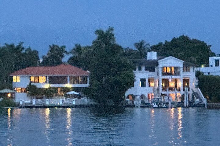 Waterfront mansions at dusk, illuminated lights reflecting on water.