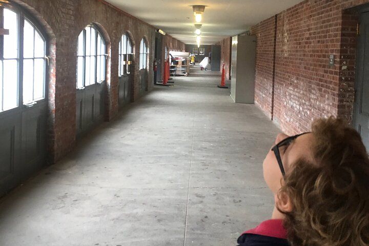Person looking upward in a long brick hallway with arched windows and doors.