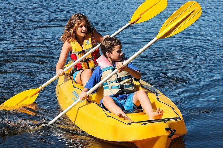 Two children in yellow kayak, paddling on water, both wearing life vests.