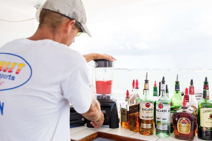 Bartender blending a drink near bottles of alcohol at a seaside bar.