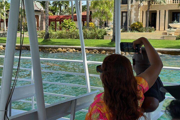 Person on a boat taking photos of a waterfront property with manicured lawn and palm trees.