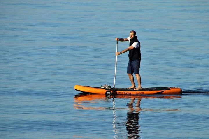 Man paddleboarding on calm blue water.