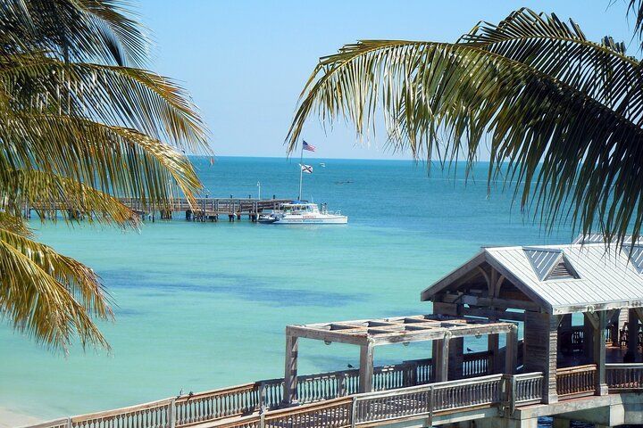Ocean view with palm trees, wooden pier, and boat under a blue sky in Key West, Florida.