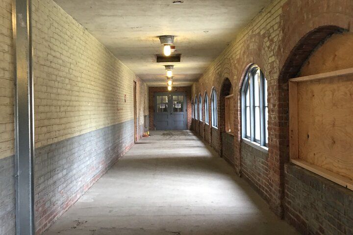 Long hallway with brick and painted walls, arched windows along one side, overhead lights.
