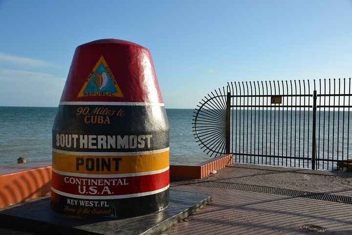 Southernmost Point buoy in Key West, Florida, painted red, black, yellow, and white, with ocean and fence in background.