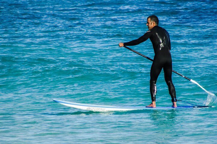 Man in wetsuit paddleboarding in turquoise water.